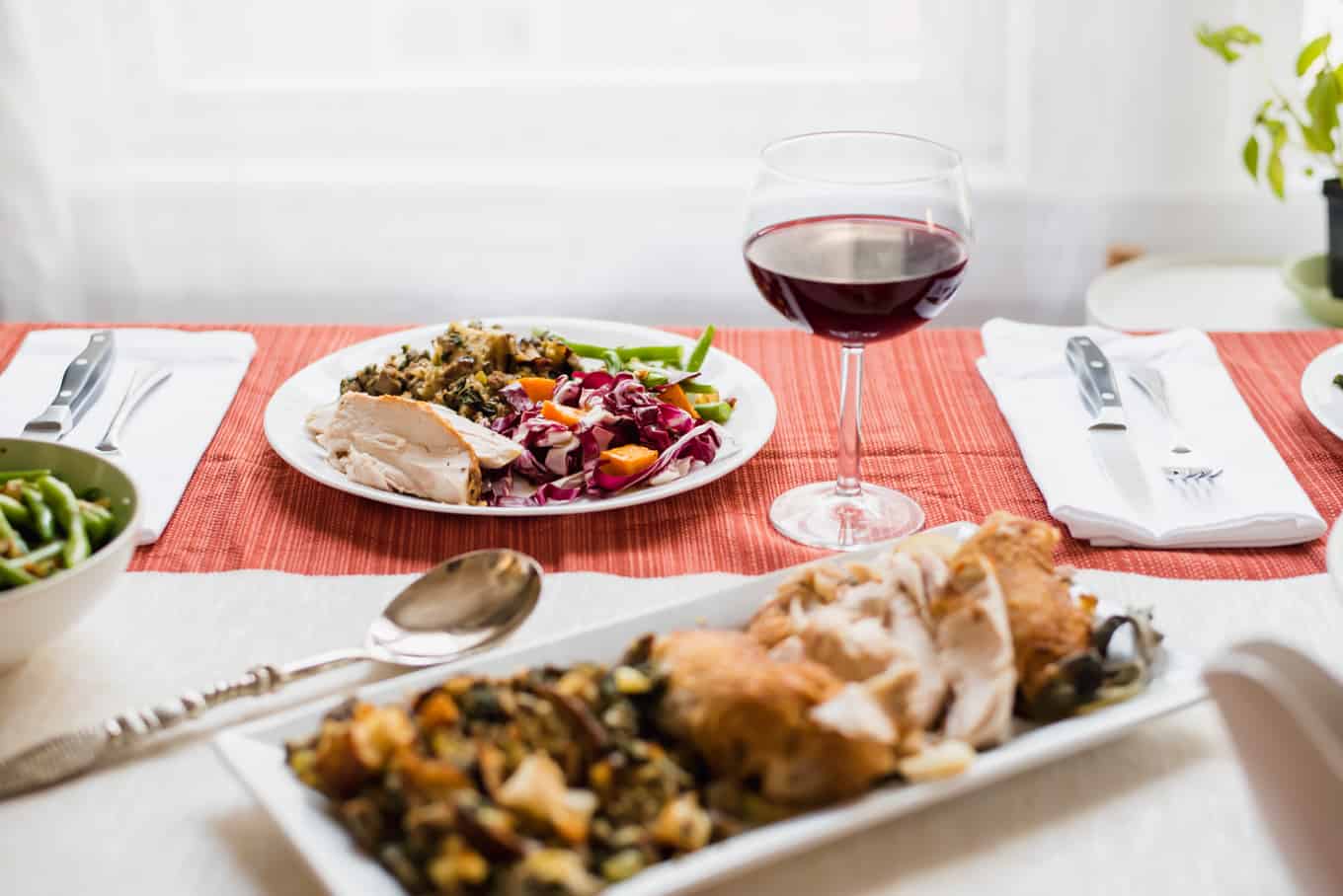 A plate of roasted turkey, salad, and stuffing on a plate with a glass of red wine.