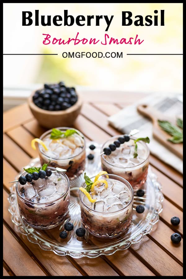 A serving tray with four glasses of blueberry basil bourbon smash. Garnished with fresh blueberries and lemon twist.