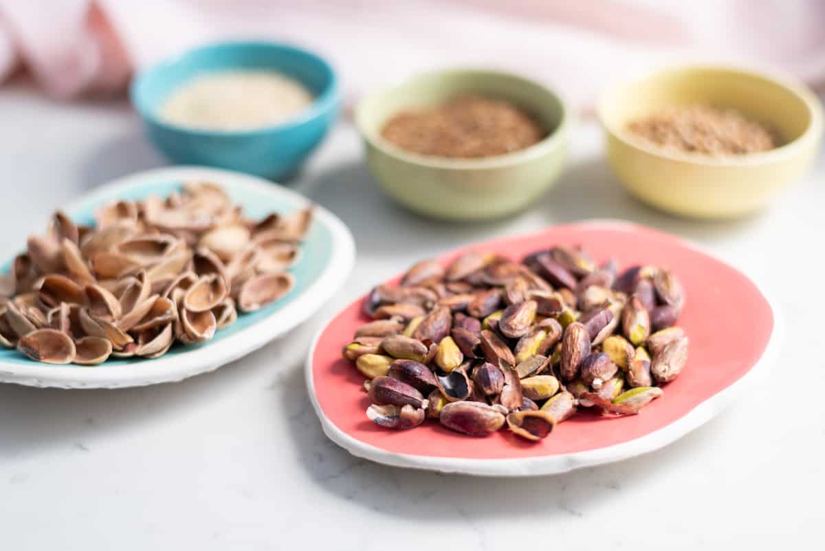 Pistachios on a small plate with pistachio shells and spices in the background.
