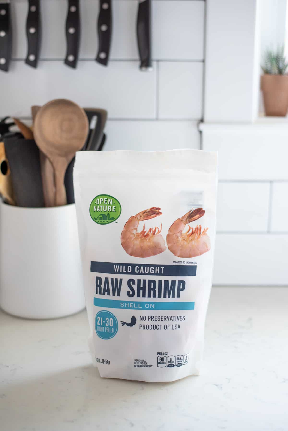 A bag of Open Nature Raw shrimp placed on a counter with utensils in the background.