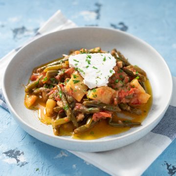 Featured image: Cooked fasolakia yiahni in a gray bowl topped with feta cheese.