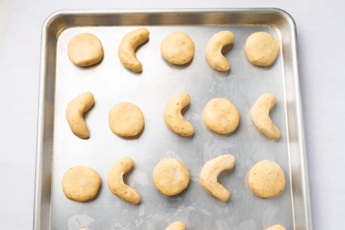 Crescent and round-shaped cookie dough on a baking sheet.