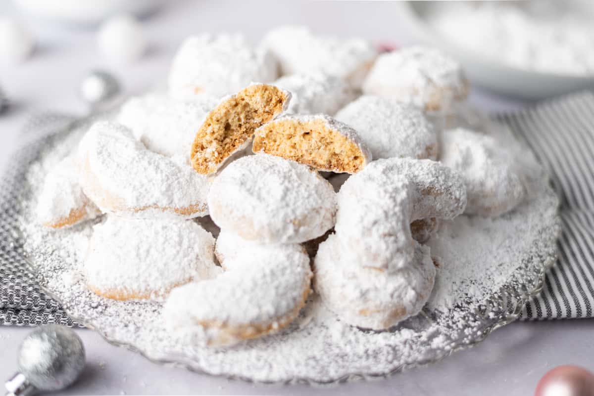 A platter of powdered sugar-covered cookies with a cookie split in half on top.