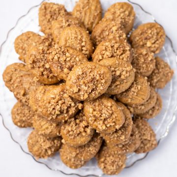 Featured image: Close up of Greek honey cookies stacked on a glass platter.