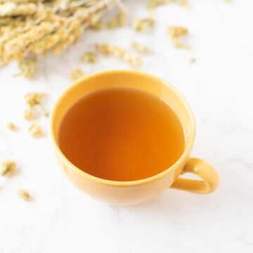 A cup of tea on a table scattered with tea leaves.