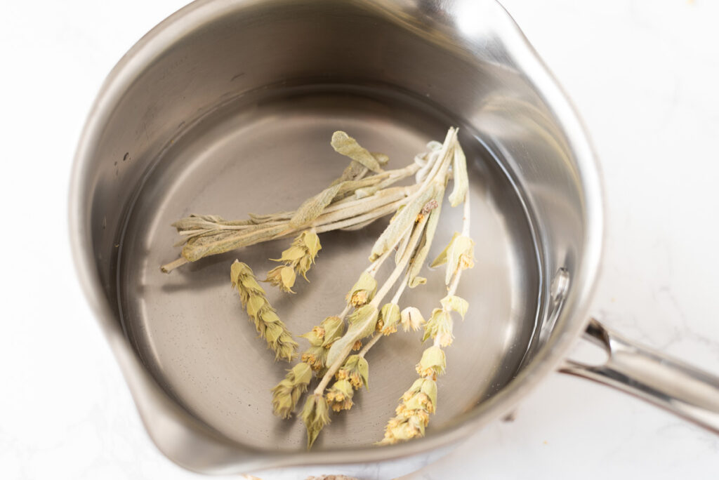 Whole tea stems and leaves steeping in a small pot of water.