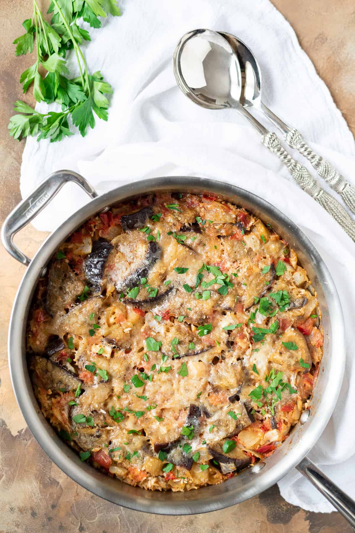 A pan of eggplant and rice casserole with serving spoons in the background.