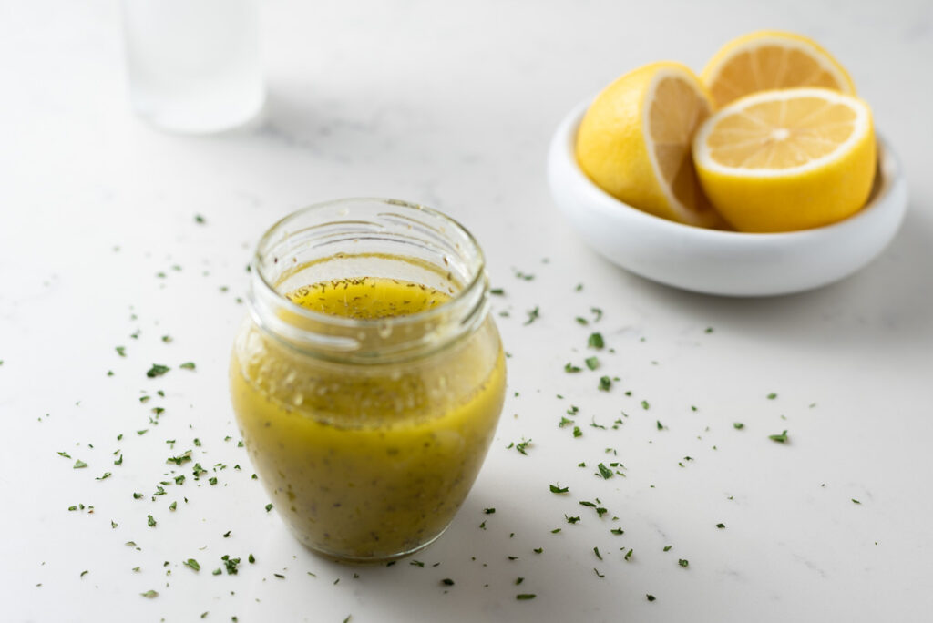 Lemon dressing in a jar with a small bowl of lemons in the background.
