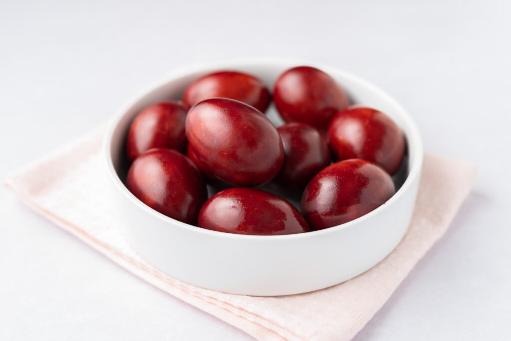 Closeup of red-dyed eggs in a white bowl.