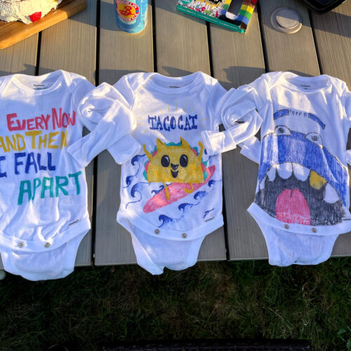 Three decorated baby onesies on a table.