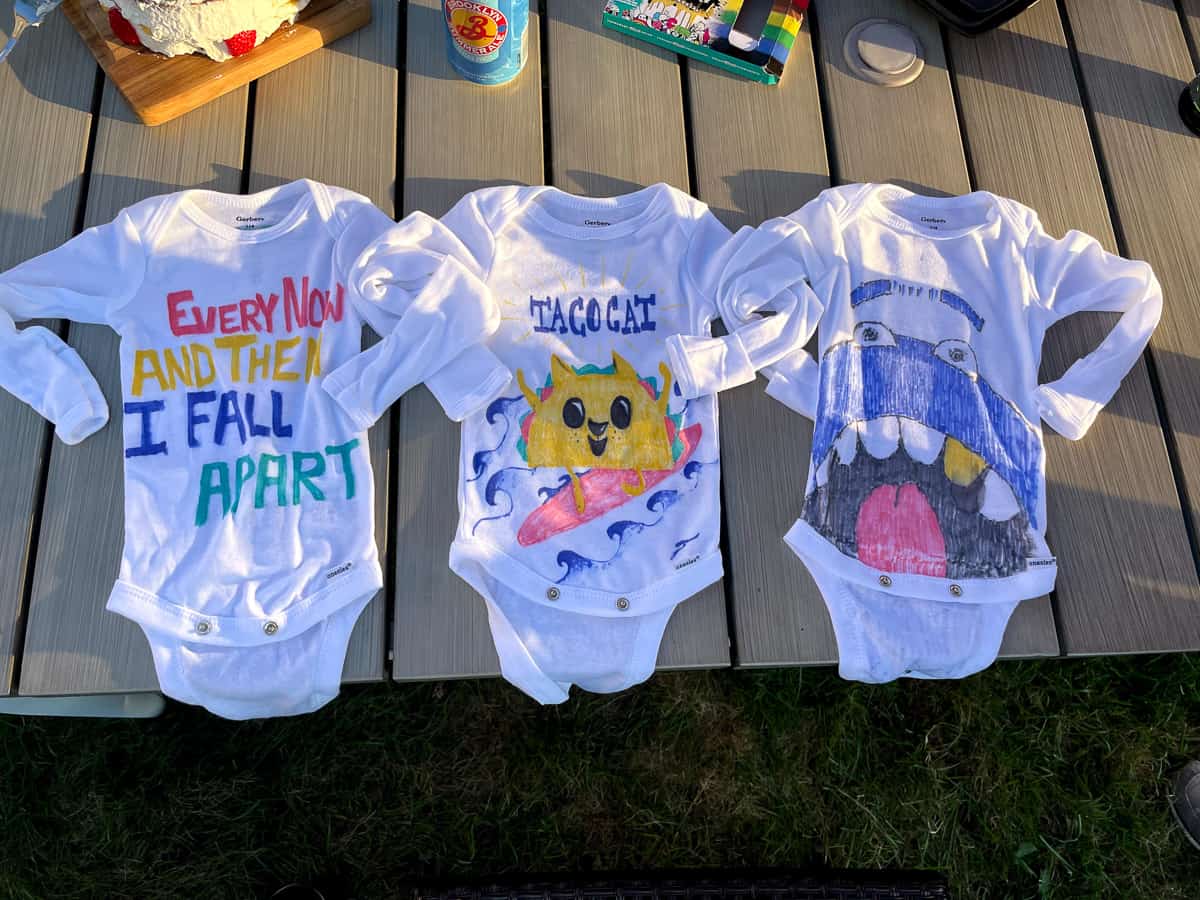 Three decorated baby onesies on a table.