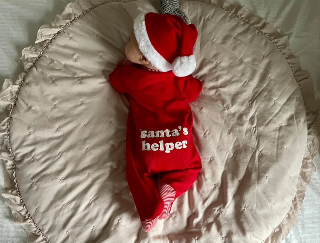 A baby in a red jumpsuit and Christmas hat.